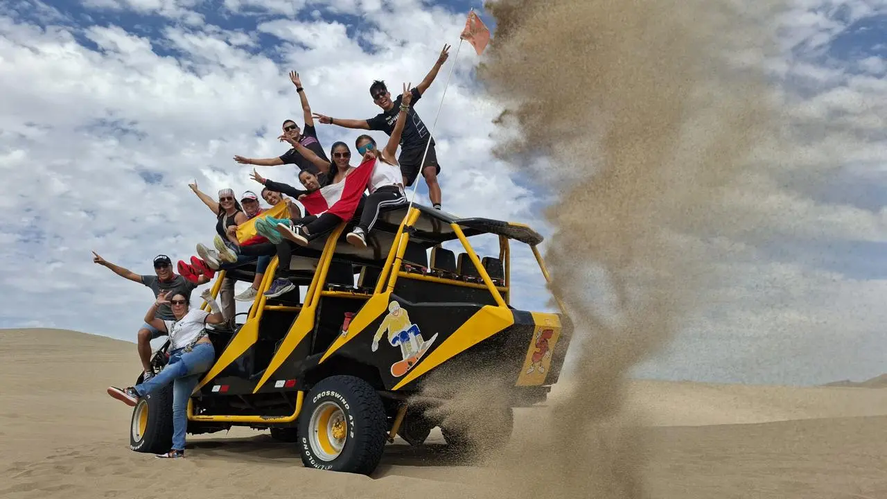 A group of excited tourists posing on top of a yellow dune buggy in the Peruvian desert sand dunes