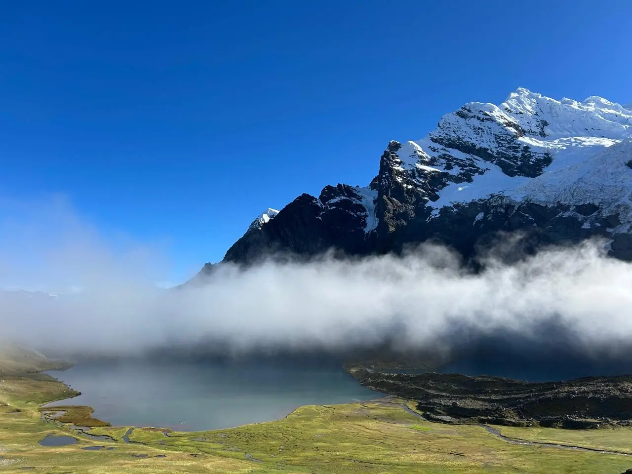 Laguna glaciar turquesa y nevado Ausangate entre nubes en el trekking Ausangate, Perú.