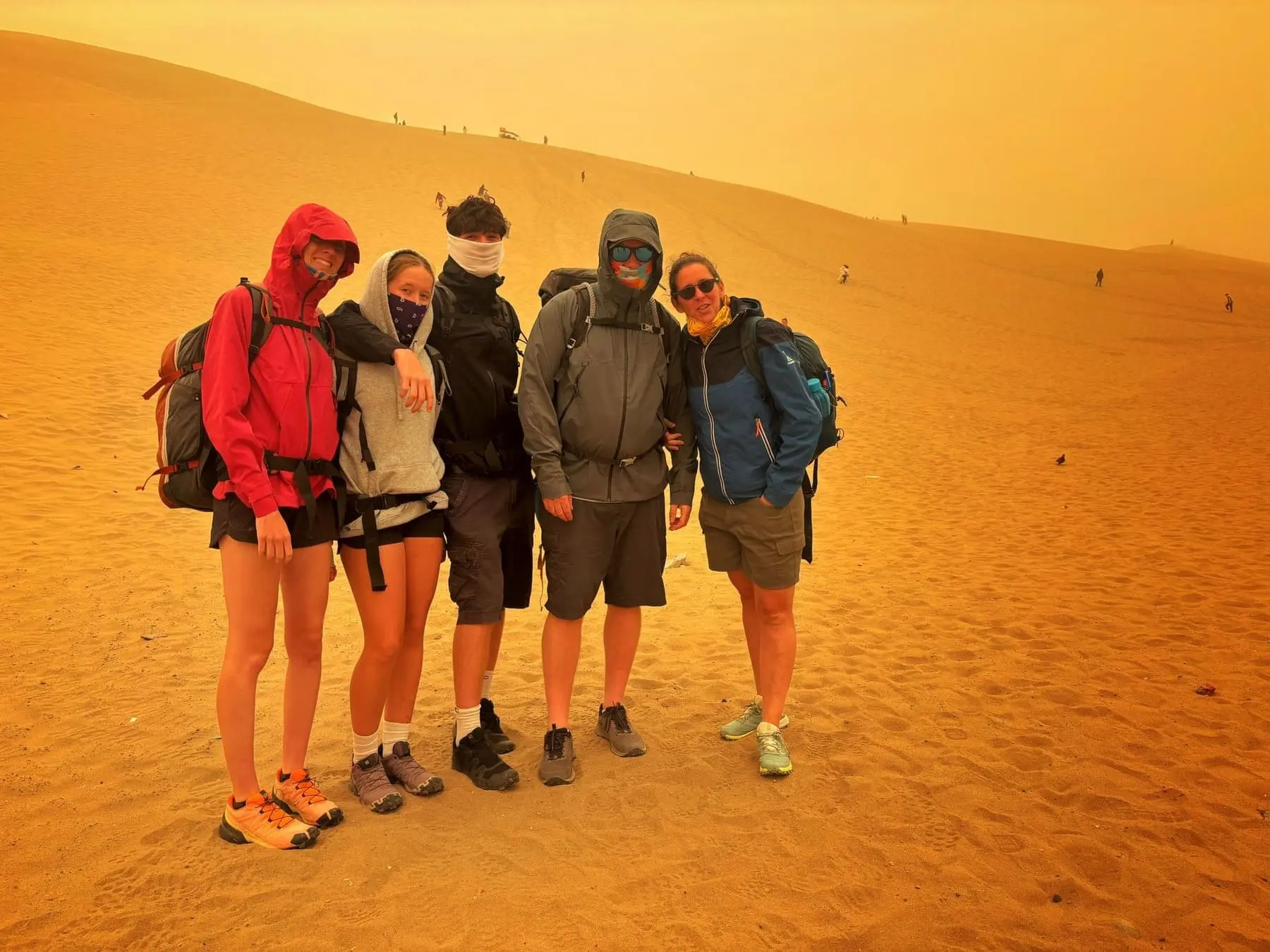 A group of five travelers in hiking gear posing on the Huacachina sand dunes with Ausangate Adventure