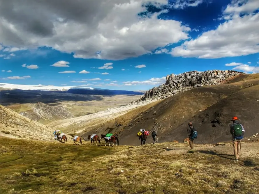 Hikers and horses crossing a remote high-altitude mountain pass during the Ausangate Sibinaqocha Trek in Peru.