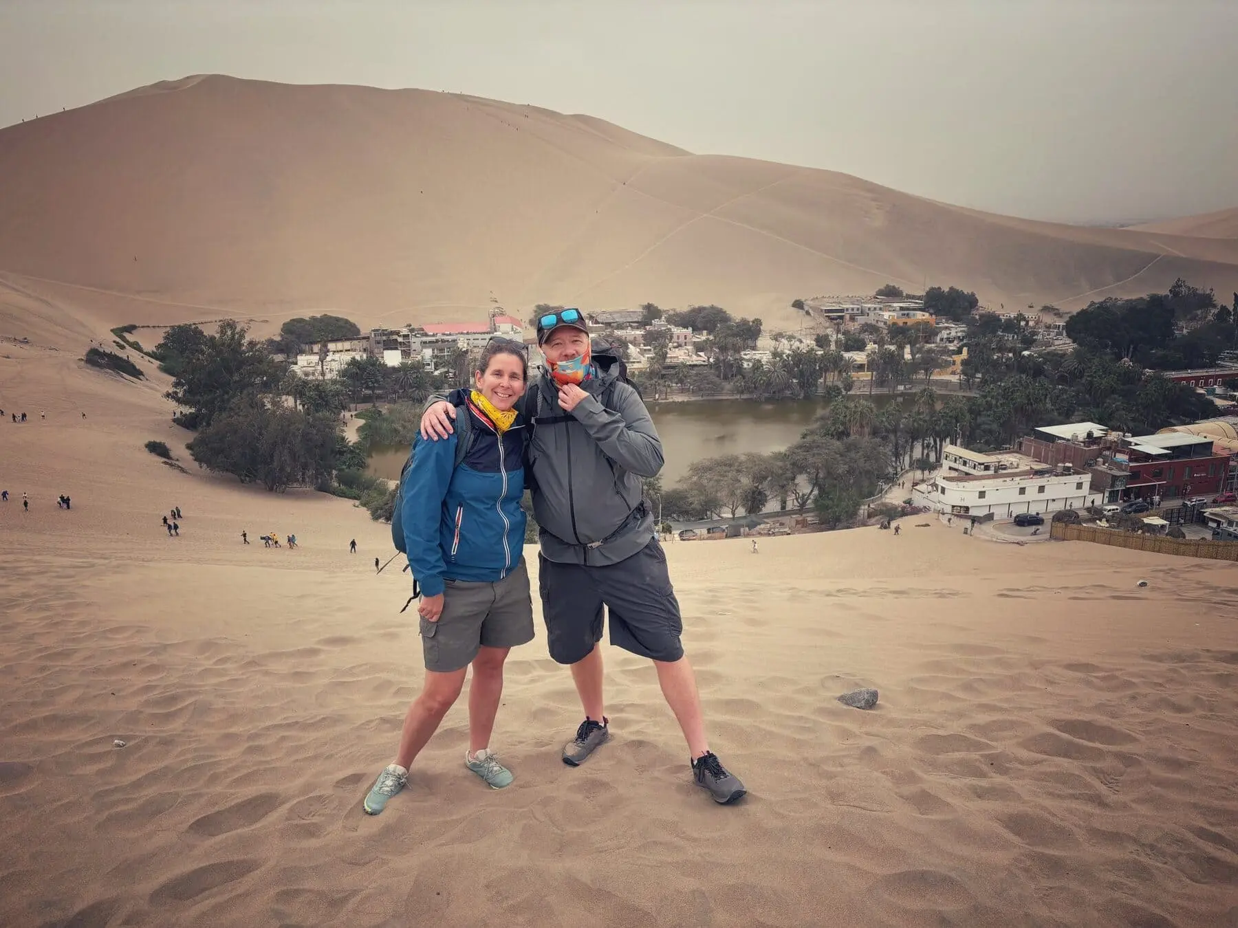 Two travelers on a desert dune overlooking the Huacachina Oasis in Peru.