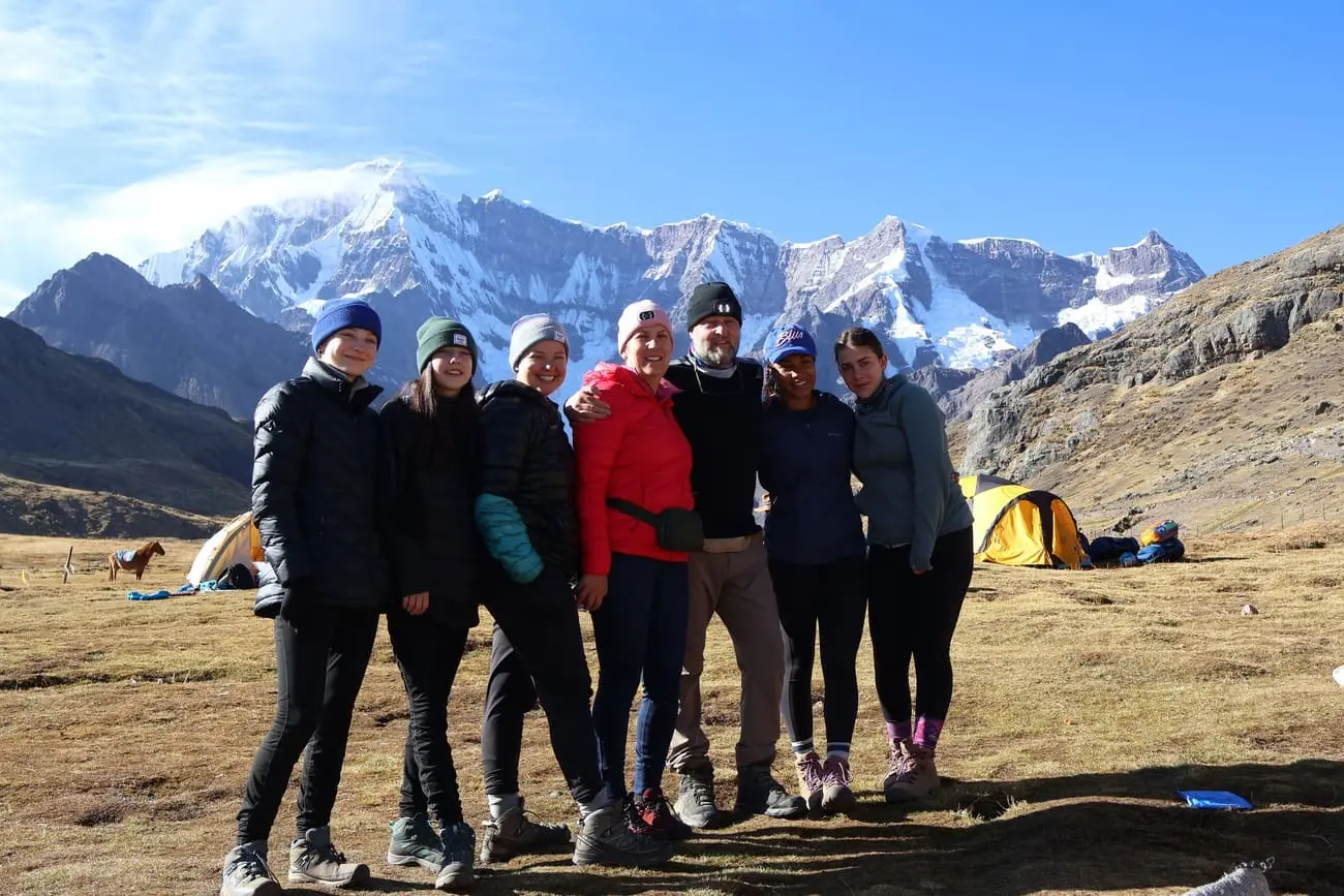 A diverse group of happy hikers with professional guide trekking on a sunny day with the snow-capped Ausangate mountain in the background. Best guided hiking tours in Cusco, Peru for adventure travelers